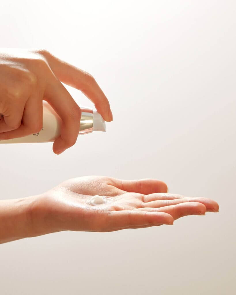 Two hands — one dispensing a small amount of liquid or lotion into the palm of the other.